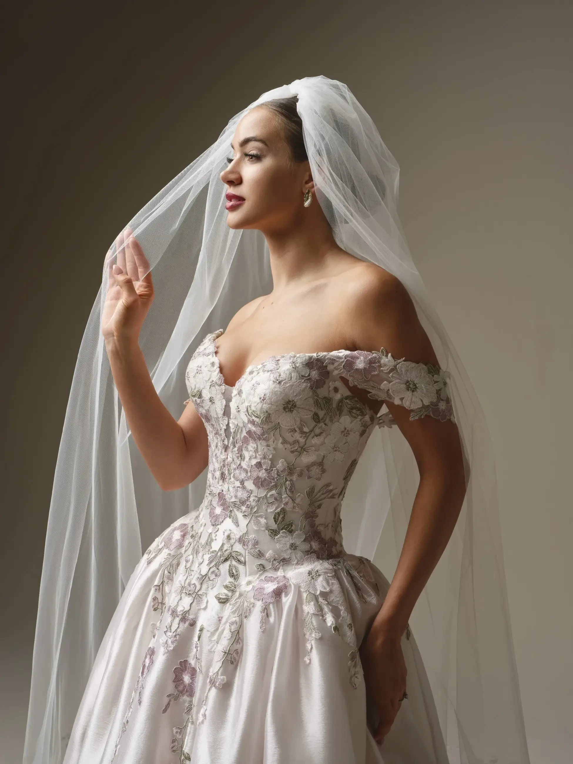 A woman in an elegant wedding dress with delicate floral details, wearing a veil and posing gracefully.