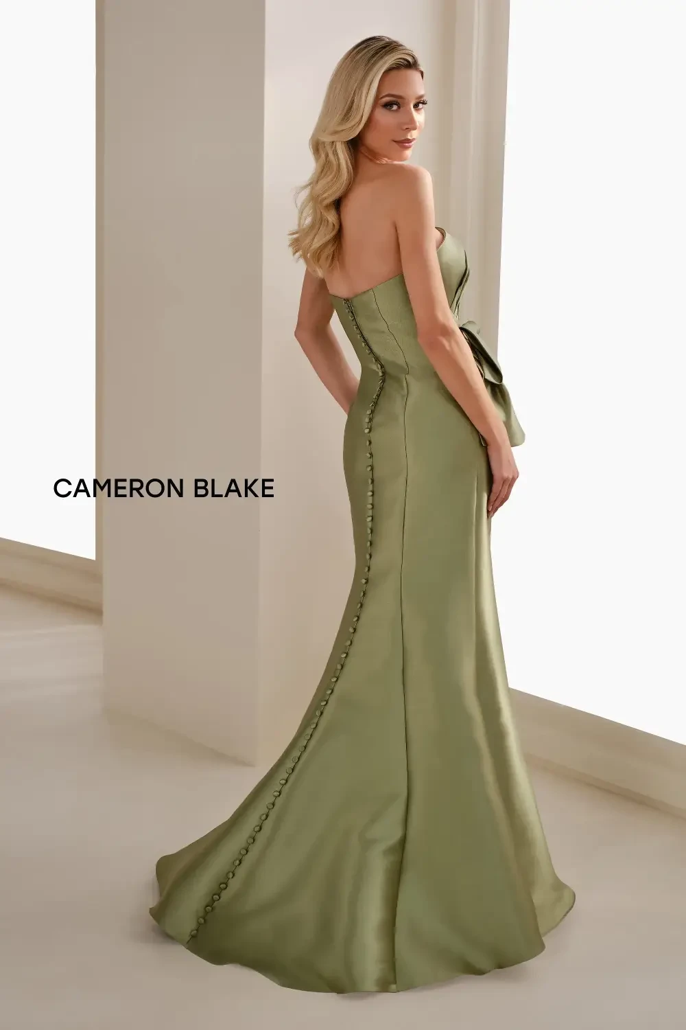 A woman in a strapless, green gown with a side bow and button detailing on the back, looking away from the camera.
