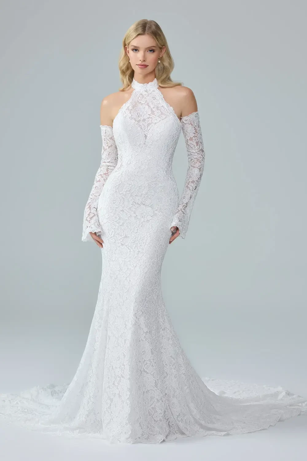 A model wearing a fitted white lace gown with long sleeves and a high neckline, standing against a light gray background.